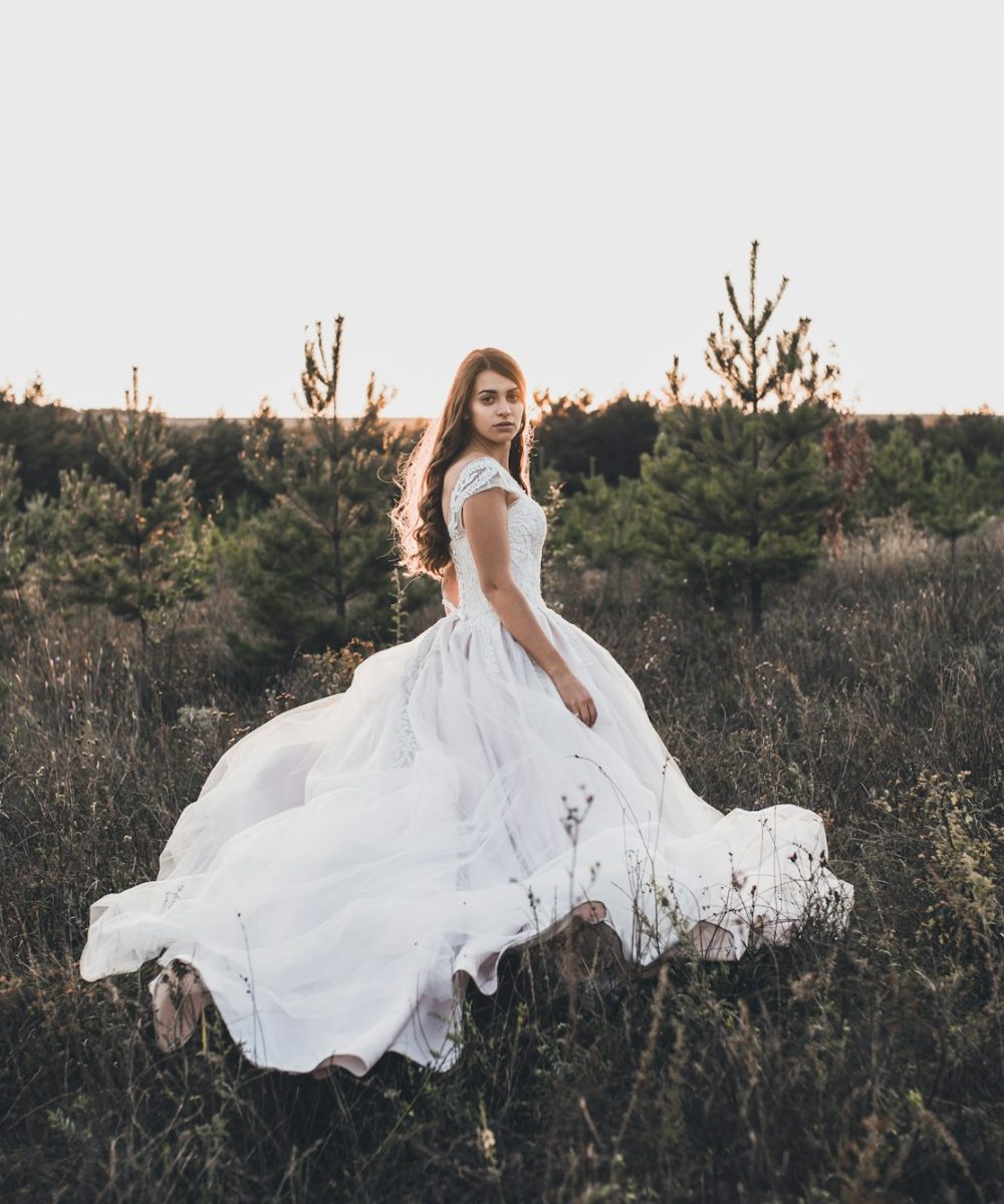 Bride in wedding white dress walking on meadow in summer at sunset