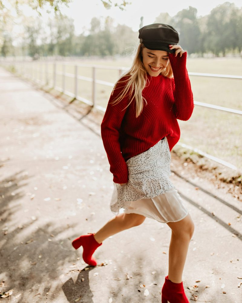 Stylish blonde in red sweater having party with great emotions outdoor. Smiling girl dancing with j